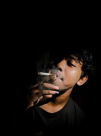 Portrait of man smoking cigarette against black background