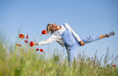 Rear view of woman with arms outstretched standing on field against clear sky