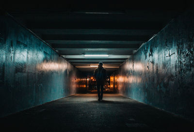 Rear view of man walking in illuminated tunnel