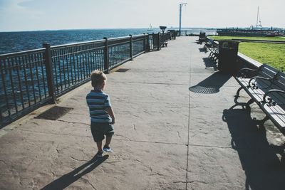 Rear view of boy walking on pier by sea against sky