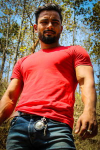 Low angle portrait of young man standing against trees