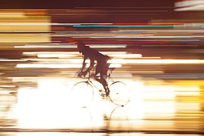Silhouette man riding bicycle with light trails on road