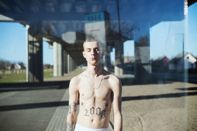 Shirtless man standing by glass in city