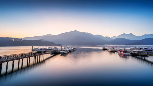 Boats moored in harbor at sunset