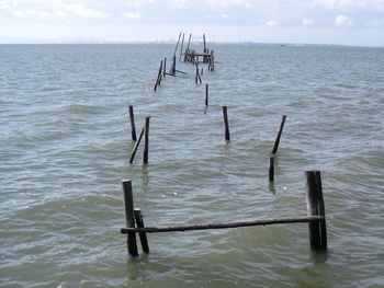 Wooden posts in sea against sky