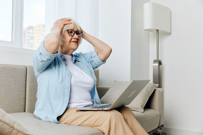 Young woman using mobile phone while sitting on sofa at home