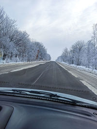 Road amidst trees against sky seen through car windshield