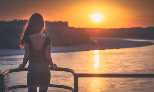 Rear view of woman looking at sea during sunset