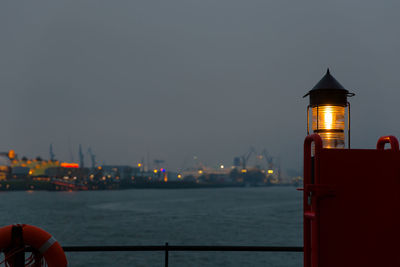 Illuminated lighthouse by elbe river against sky in city at dusk