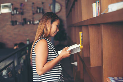 Side view of woman reading book while standing at library