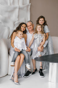 Happy family of five is posing for photo in front of couch. people are wearing silver dresses 
