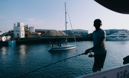 Man standing in harbor by sea against sky