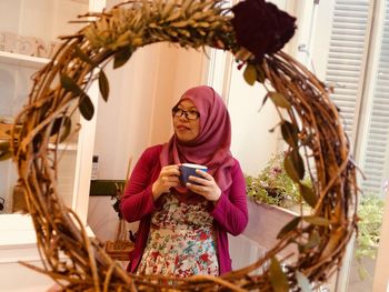 Woman with coffee cup seen through wreath