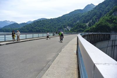 People on riverbank by mountains against sky