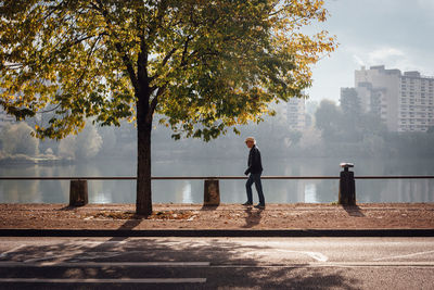 Side view of man walking by railing amidst road and lake