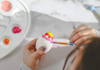 Little caucasian girl paints an easter egg with a brush with yellow red acrylic paint