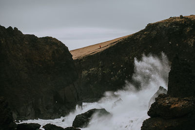 Scenic view of sea by mountain against sky