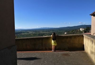 Rear view of girl looking at landscape while standing against retaining wall