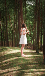 Full length of woman standing by tree in forest