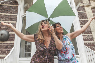 Couple of two attractive fifty year old women with umbrella in front of french villa on a rainy day