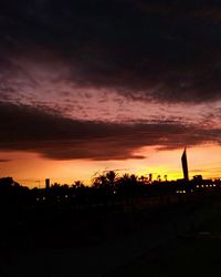 Silhouette trees on field against dramatic sky during sunset