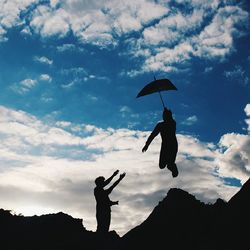 Low angle view of woman jumping against cloudy sky