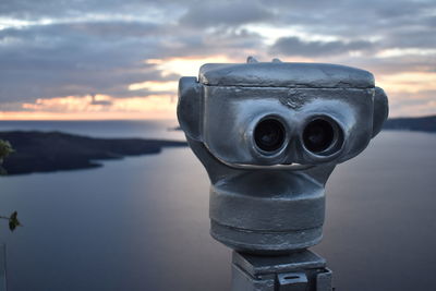 Close-up of coin-operated binoculars by sea against sky during sunset