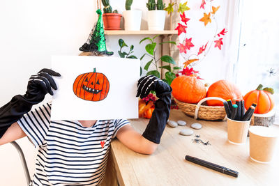 A child shows his drawing for halloween, sitting at a desk by the window, surrounded by pumpkins.