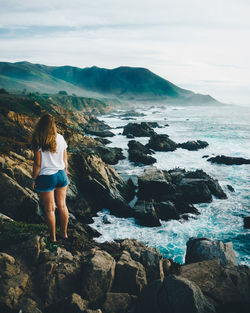 Rear view of woman standing at rocky beach