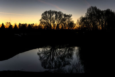 Silhouette trees by lake against sky at sunset