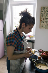 Woman wearing apron cutting fruits while preparing food in kitchen
