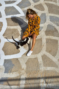 High angle view of young woman sitting with cat on walkway 