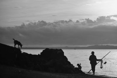 Silhouette man with dog standing at beach against sky