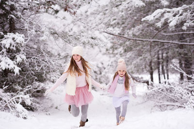 Full length of sisters holding hands walking on snow covered land