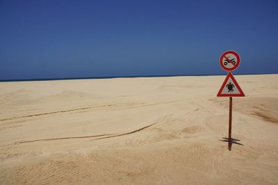 Road sign on beach against clear blue sky