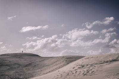 Distant view of person standing on sand dunes against sky