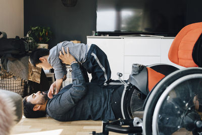 Side view of father playing autistic son while lying on floor at home