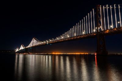 Illuminated bridge over river against sky at night