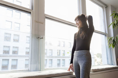 Side view of young woman standing against window at home