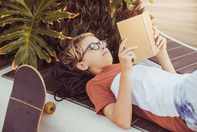 Boy reading book while lying down by plants