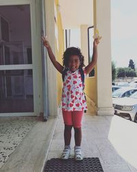 Full length portrait of smiling girl standing against built structure