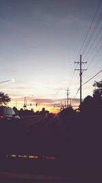 Silhouette of electricity pylons against sky at sunset