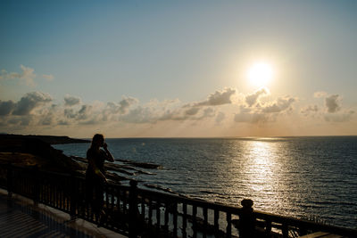 Silhouette people standing by railing against sea during sunset