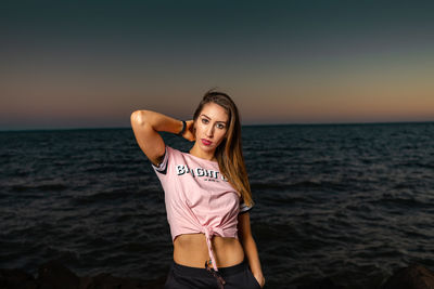 Portrait of woman standing at beach against sky during sunset