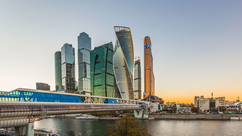 Modern buildings by river against clear sky