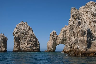 Rock formations in sea against clear blue sky