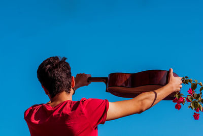 Rear view of man drinking water against blue sky