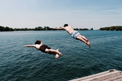 Shirtless friends jumping into river against sky