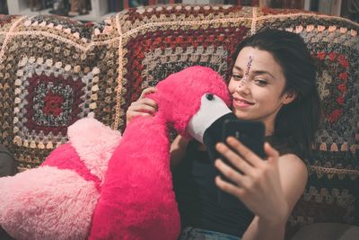 Smiling young woman taking selfie with stuffed toy on sofa at home