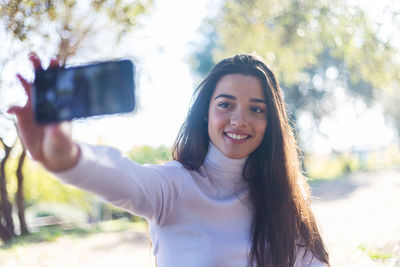 Smiling young woman taking selfie from mobile phone